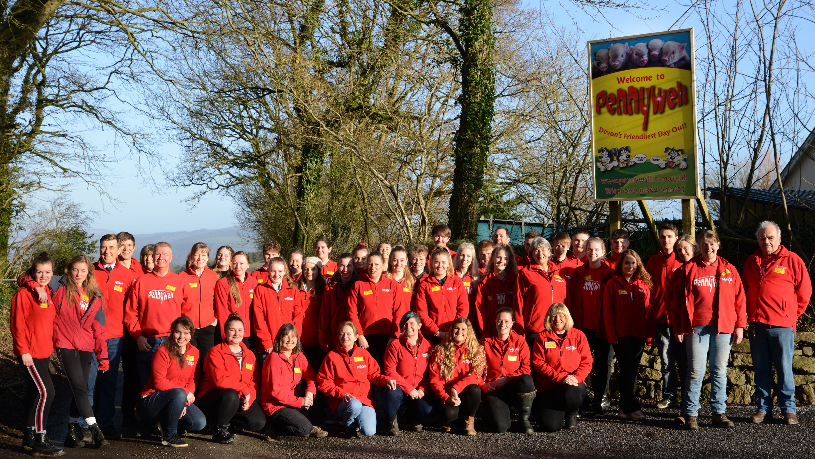 Group of people wearing red jackets standing outdoors near Pennywell sign with trees in background