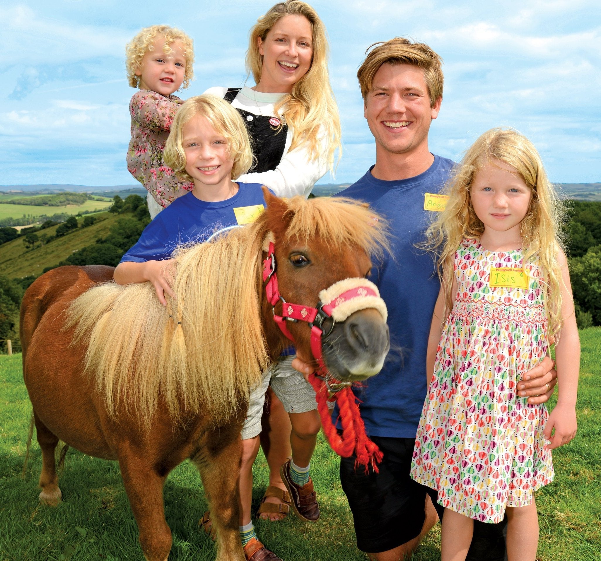 Family of two adults and three children with a small brown pony in a green field under blue sky
