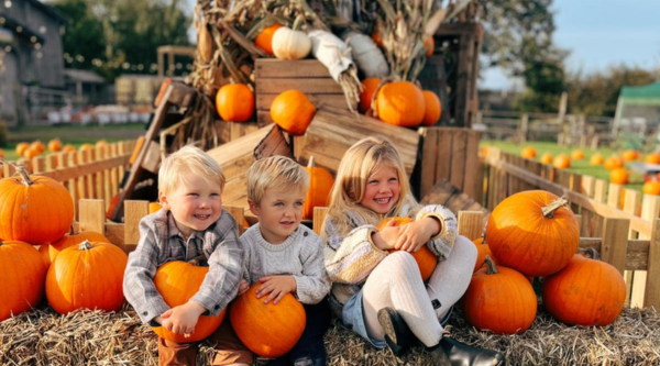 Three children sitting among orange pumpkins on hay bales at a pumpkin festival