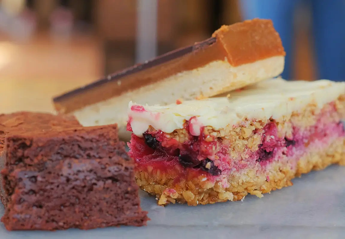 three types of cake: a chocolate brownie, a fruity layered slice, and a caramel shortcake on a grey surface