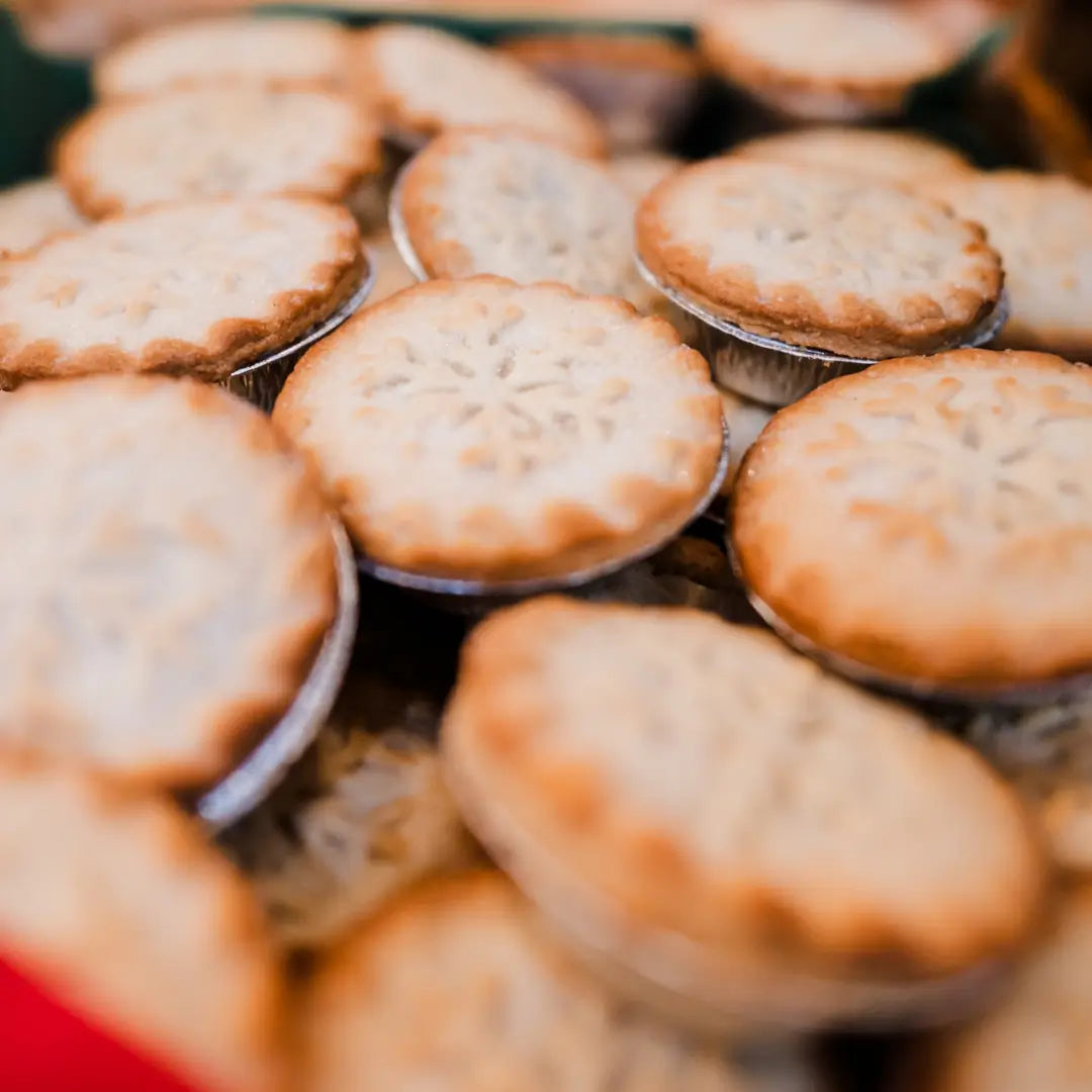 a close-up of several golden-brown mince pies arranged closely together, showing their decorative tops