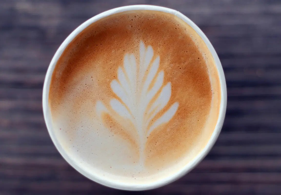 a close-up of a latte with a leaf-shaped foam design on top, set against a wooden background