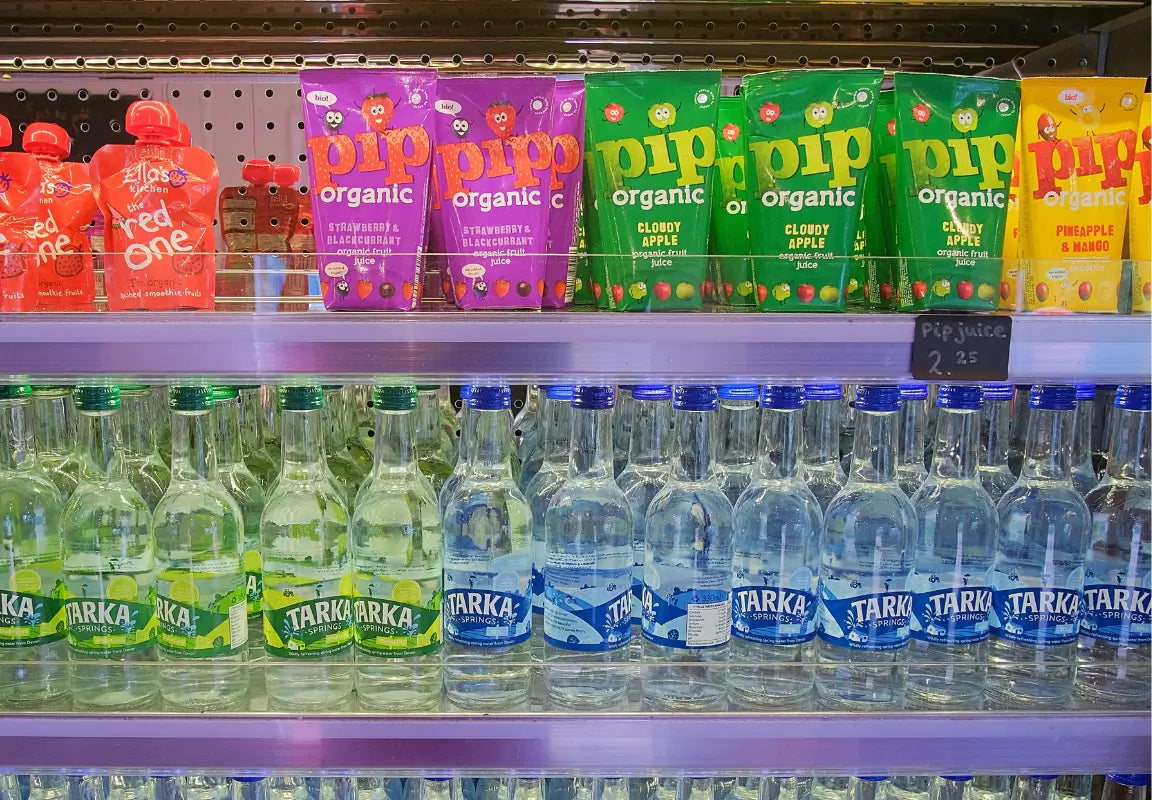 shelves displaying various fruit juices and bottled water, including pip organic and tarka brands