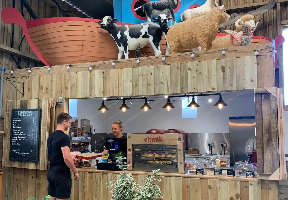 a café counter with a man ordering from a woman, decorated with animal sculptures and a menu board on the wall