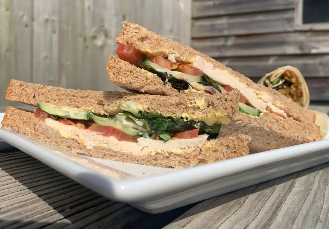 two slices of wholemeal sandwich filled with chicken, lettuce, tomato, cucumber, and mayonnaise on a plate