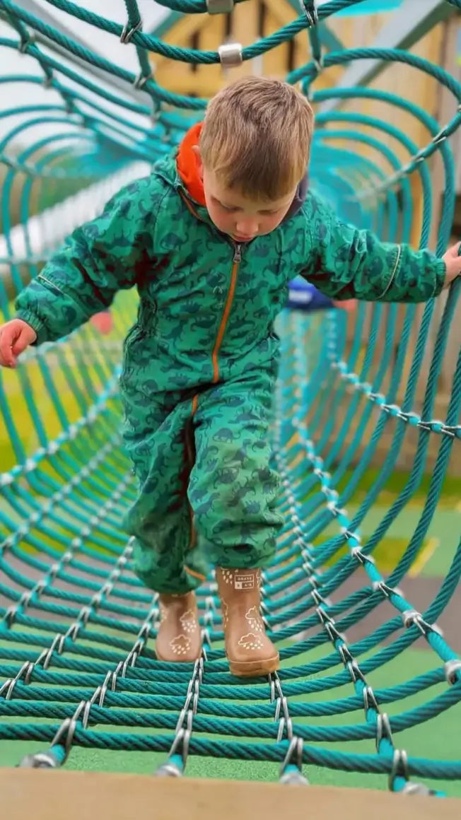 a young child in a green camouflage suit walks carefully on a rope bridge at a playground