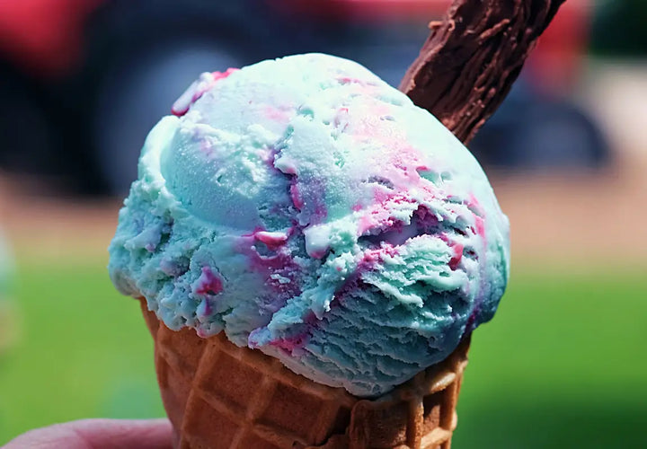 a close-up of a waffle cone filled with blue and pink swirled ice cream, with a chocolate flake on top