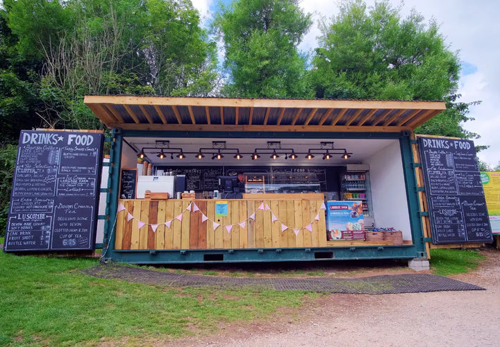 food and drink kiosk with wooden counter and chalkboard menus, surrounded by greenery and bunting.