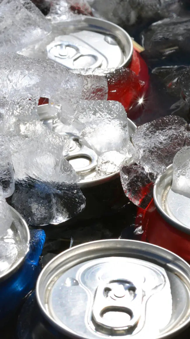 cans of drink in ice, with some visible in red and blue, surrounded by crushed ice on a dark surface