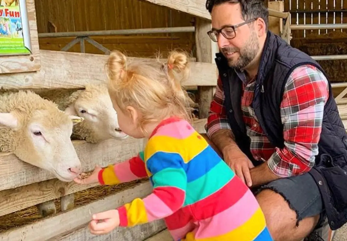 a young child in a striped outfit feeds sheep while an adult watches in a farm setting