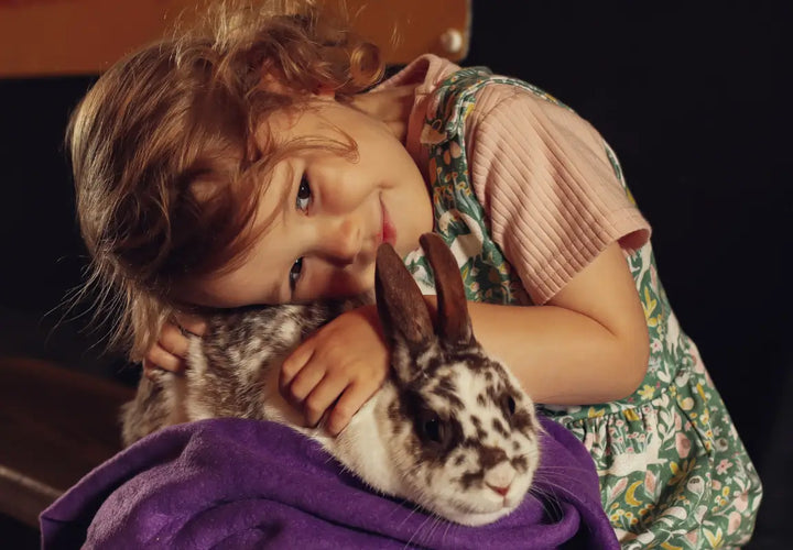 a young girl cuddles a spotted rabbit, resting her head on it while wrapped in a purple blanket