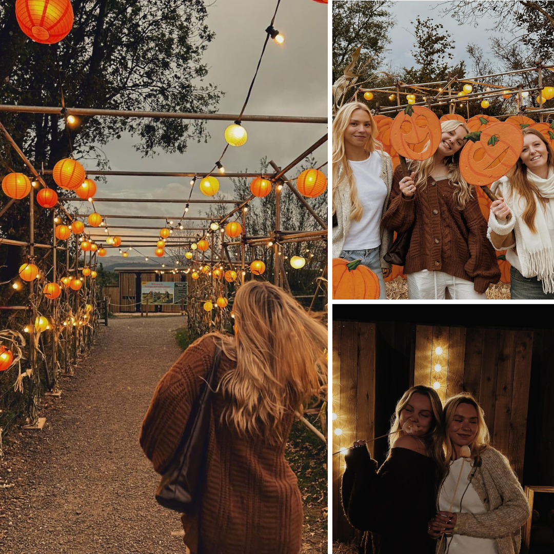A pathway adorned with orange lanterns, featuring three women posing with pumpkin cutouts and fairy lights.