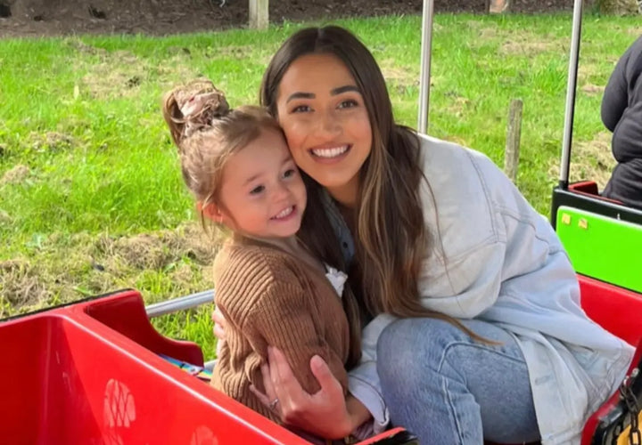 a young girl and a woman smile together while sitting in a red ride, with green grass in the background