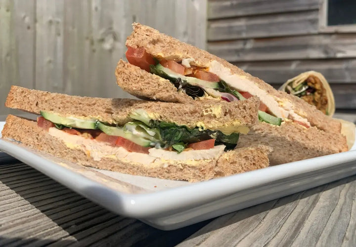 two slices of wholemeal sandwich filled with chicken, lettuce, tomato, cucumber, and mayonnaise on a plate
