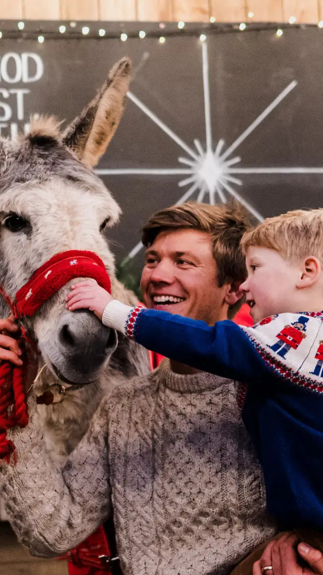 a man and a child interact with a donkey, both smiling, in a festive setting with decorations in the background