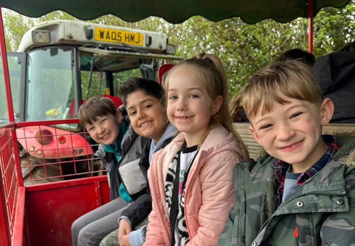 Four children smiling while sitting on a red tractor, surrounded by greenery.