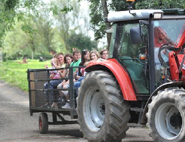 Red tractor with large tyres pulling a trailer carrying seven people on a rural dirt path